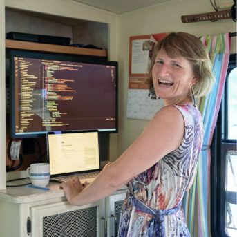 Person in dress smiling in front of laptop and monitor