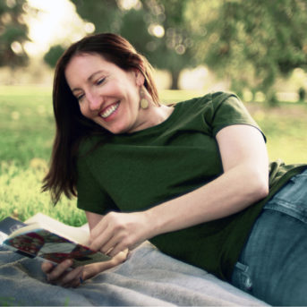 Melanie reading a book while laying on grass.